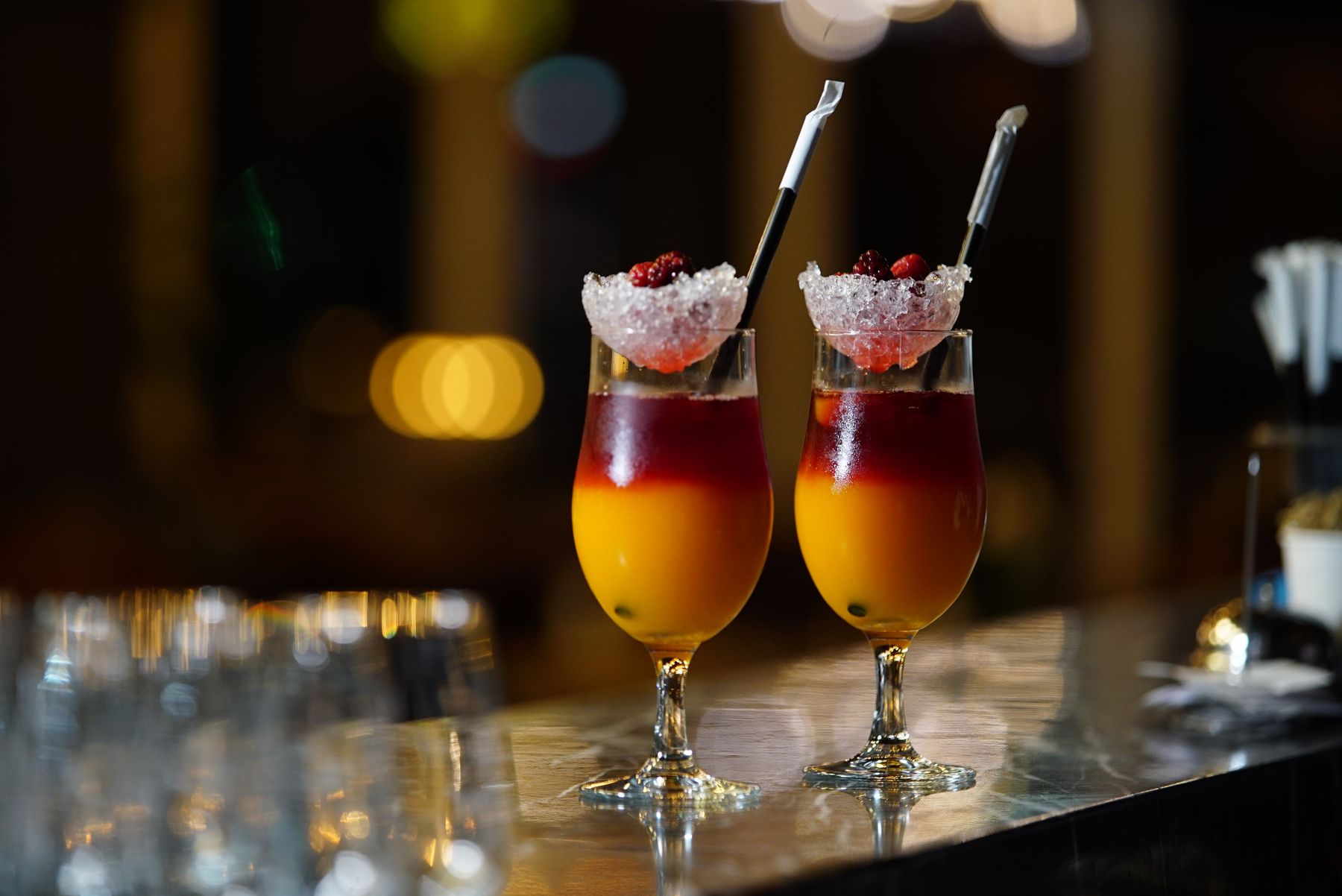 Two cocktails with berries and ice on a bar counter